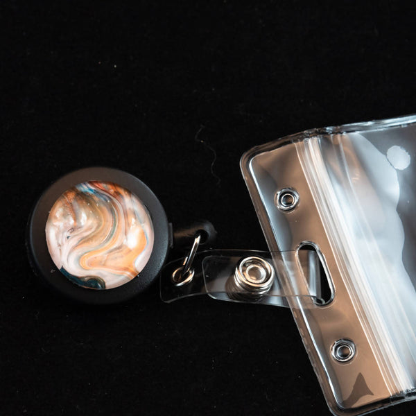 Retractable badge holder with unique acrylic painted cabochon decoration.