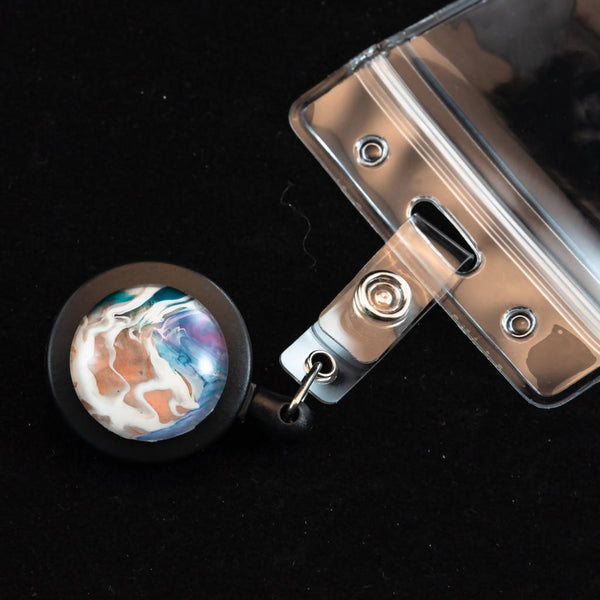 Retractable badge holder with unique acrylic painted cabochon decoration.